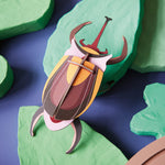 Studio roof slotting cardboard elephant beetle craft model climbing over some model leaves on a blue background