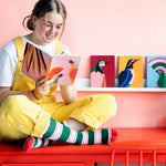 Girl sat on top of a red desk writing inside a Studio Roof Paradise Bird eco-friendly Notebook