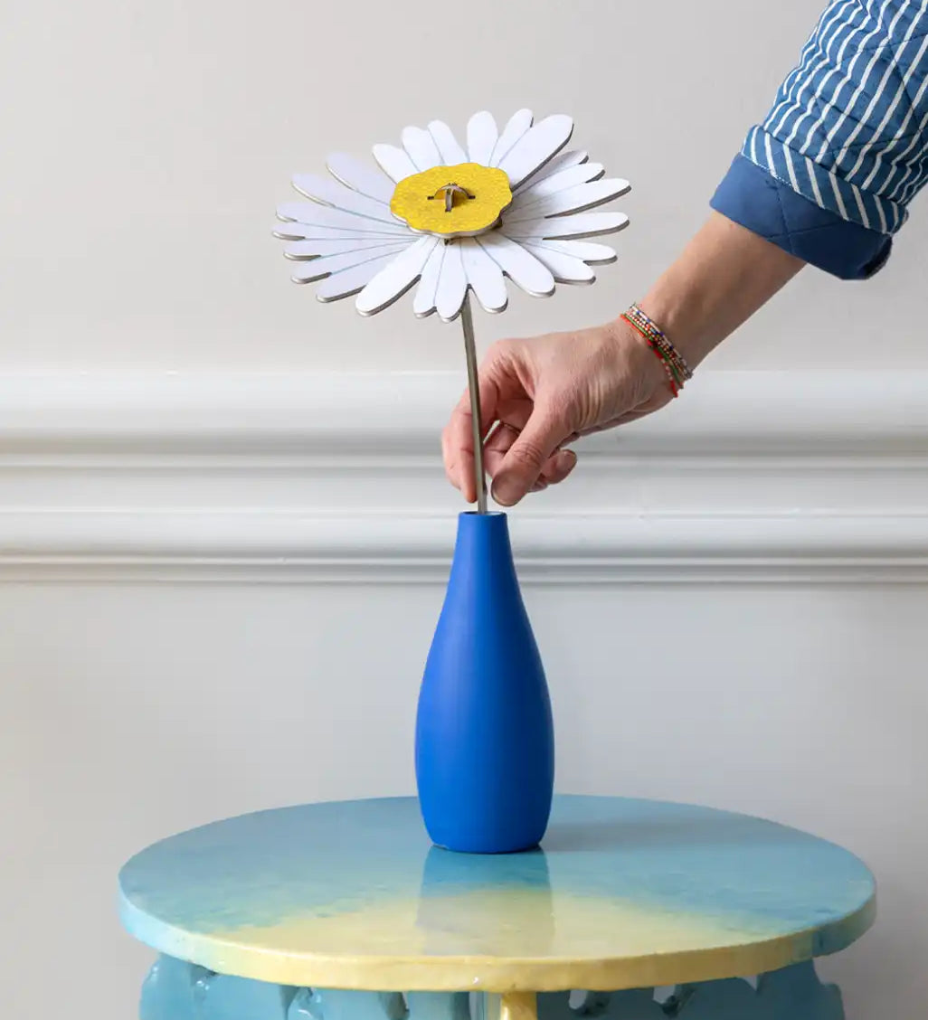 Studio Roof daisy everlasting flower cardboard flower decoration shown built and being placed in a blue vase.