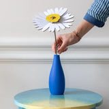 Studio Roof daisy everlasting flower cardboard flower decoration shown built and being placed in a blue vase.