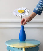 Studio Roof daisy everlasting flower cardboard flower decoration shown built and being placed in a blue vase.