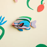 Studio Roof plastic-free Fairy Wrasse card wall decoration on a beige wall next to some green painted plants