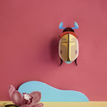 Studio Roof Lemon Fruit Beetle decoration hung up on a pinkish red painted wall
