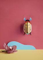 Studio Roof Lemon Fruit Beetle decoration hung up on a pinkish red painted wall