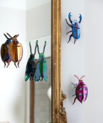 Studio Roof 3D cardboard insects displayed on a wall showing a Cuprum beetle, jade grasshopper, azure stag beetle and a lumen pink beetle model