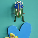 Studio Roof Mimela Scarab Beetle decoration hung up on a green painted wall