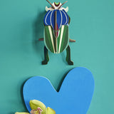 Studio Roof Mimela Scarab Beetle decoration hung up on a green painted wall
