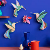 Studio Roof Dance of Hummingbirds Paradise Bird Set wall art kit assembled and displayed on a blue wall.