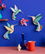 Studio Roof Dance of Hummingbirds Paradise Bird Set wall art kit assembled and displayed on a blue wall.