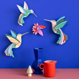 Studio Roof Dance of Hummingbirds Paradise Bird Set wall art kit assembled and displayed on a blue wall.