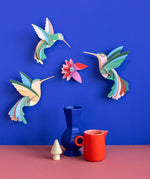 Studio Roof Dance of Hummingbirds Paradise Bird Set wall art kit assembled and displayed on a blue wall.