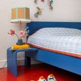 Studio ROOF Dance of Hummingbirds 3D cardboard wall art displayed above a bed, colourful hummingbird wall decorations flying around a flower in a bright bedroom setting.