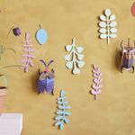 Studio Roof card craft bugs hanging on a yellow wall next to a potted plant