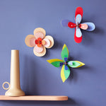 3 Studio Roof craft flowers hung on a purple wall next to a beige shelf and candle holder