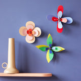 3 Studio Roof craft flowers hung on a purple wall next to a beige shelf and candle holder