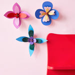 3 Studio Roof plastic-free craft flowers hung on a pink wall next to a red painted shelf