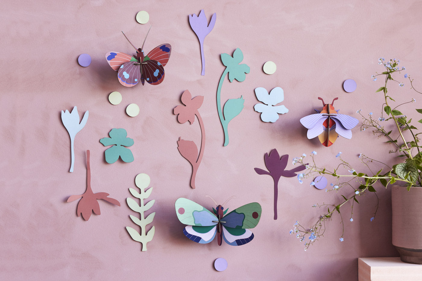 Studio Roof Winged Medley DIY wall decorations on a pink wall next to a large potted plant