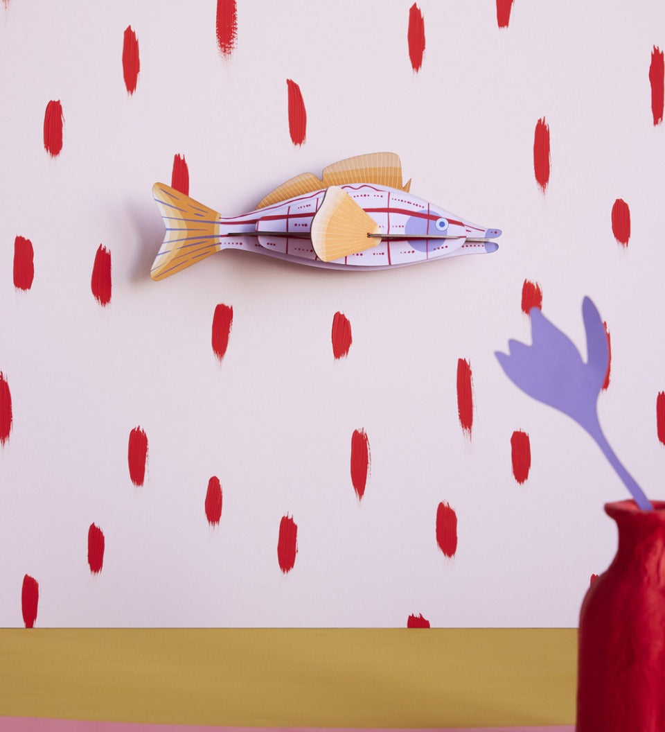 Studio Roof plastic-free card fish wall decoration hanging on a pink and red wall next to a red potted plant