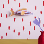 Studio Roof plastic-free card fish wall decoration hanging on a pink and red wall next to a red potted plant