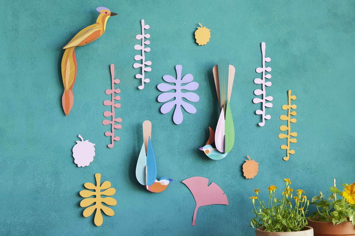 Studio Roof plastic-free card bird wall decorations on a blue wall next to some potted plants