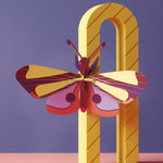 Studio roof slotting cardboard butterfly decoration climbing on a yellow arch in front of a purple background