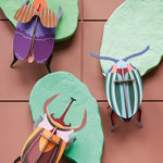3 Studio roof slotting craft model beetles climbing on some green model leaves on a brown background