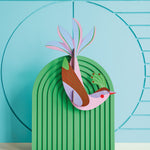 Studio roof eco-friendly maui bird card model attached to a green stand in front of a blue patterned wall