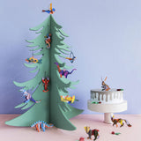 Studio Roof eco-friendly cardboard ornaments hanging from a wooden christmas tree in front of a blue wall