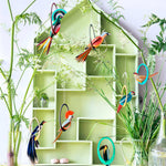 Studio Roof paradise Bird pop-out cardboard decorations hanging from potted plants in front of a green wooden house shelf