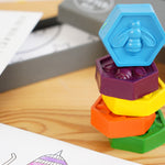 Close up of the hexagonal crayon bug bee crayons set stacked in a tower on a wooden background next to their grey box