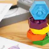 Close up of the hexagonal crayon bug bee crayons set stacked in a tower on a wooden background next to their grey box