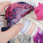 Close up of a hand reaching out to hold the Crayon Bug fantasy crayons on a colouring book