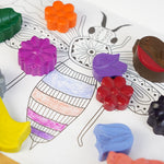Close up of the crayon bug rainbow gardens handmade wax crayon set laid out on a white colouring page