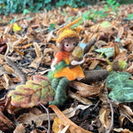 The fairy from The Makerss Official Flower Fairies™️ - Acorn Fairy Needle Felt Kit made and placed on the leaf covered ground outdoors. 