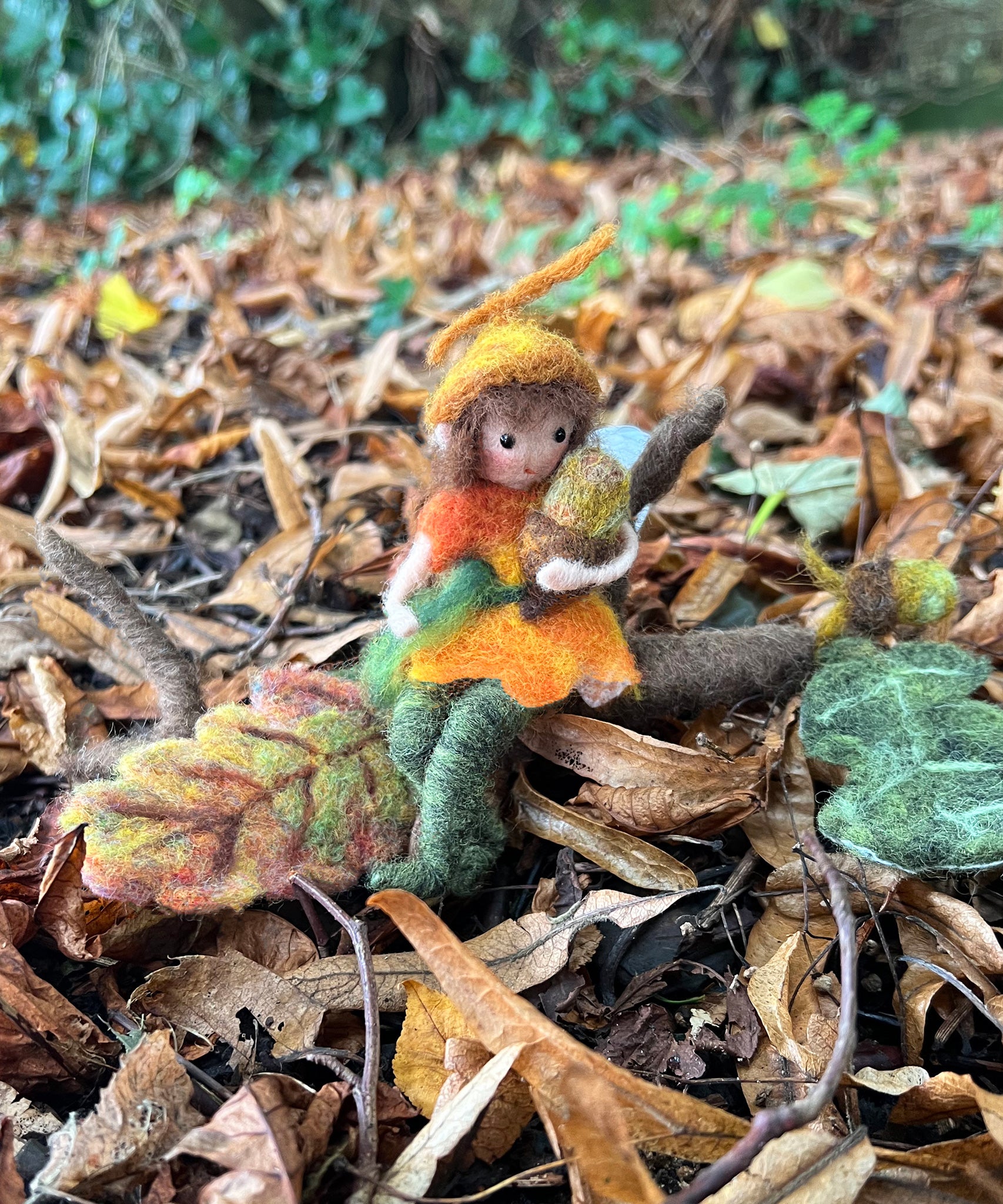 The fairy from The Makerss Official Flower Fairies™️ - Acorn Fairy Needle Felt Kit made and placed on the leaf covered ground outdoors. 