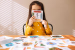 Child holding up a card with the letter S for snake on from the The Phive Enchanting Learning Phonics & Storytelling Cards - Set 1 with all the other cards laid out on the table in front of them