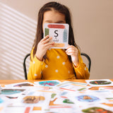 Child holding up a card with the letter S for snake on from the The Phive Enchanting Learning Phonics & Storytelling Cards - Set 1 with all the other cards laid out on the table in front of them