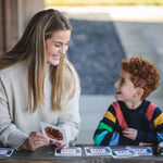 An adult sitting next to a child with a The Phive Enchanting Learning Phonics & Storytelling Card Set laid out in front of them