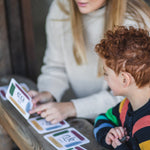 An adult sitting next to a child with a The Phive Enchanting Learning Phonics & Storytelling Card Set laid out in front of them