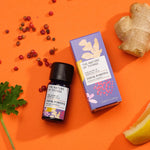Think Positive pure essential oil blend in a blue glass bottle next to a decorative purple cardboard box, with peppercorns, ginger, lemon and geranium on an orange background. 