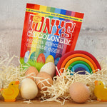 Tonys chocolonely fairtrade mini chocolate easter eggs in the mixed flavours pack on a pile of straw next to a grimms rainbow and some wooden eggs