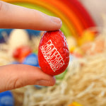 Close up of a hand holding a Tonys chocolonely egg-stra special mini chocolate easter egg in front of a grimms rainbow