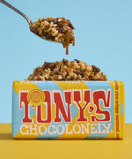 A bar Tony's Chocolonely Fairtrade Milk Rice Crispy Caramel chocolate with a pile of chocolate caramel covered crispies in the background. 