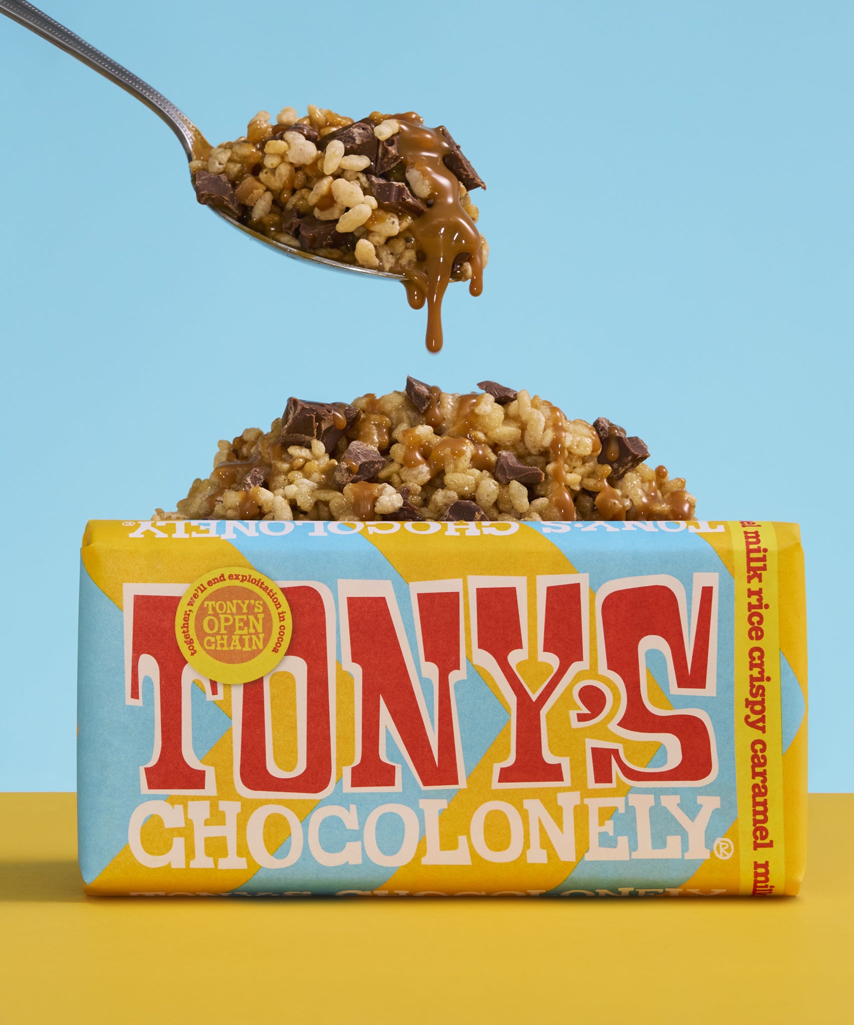 A bar Tony's Chocolonely Fairtrade Milk Rice Crispy Caramel chocolate with a pile of chocolate caramel covered crispies in the background. 