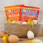 Tonys chocolonely eco-friendly mini easter egg chocolate pouches in a basket surrounded by small wooden eggs and chick toys