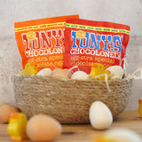 Tonys chocolonely eco-friendly mini easter egg chocolate pouches in a basket surrounded by small wooden eggs and chick toys