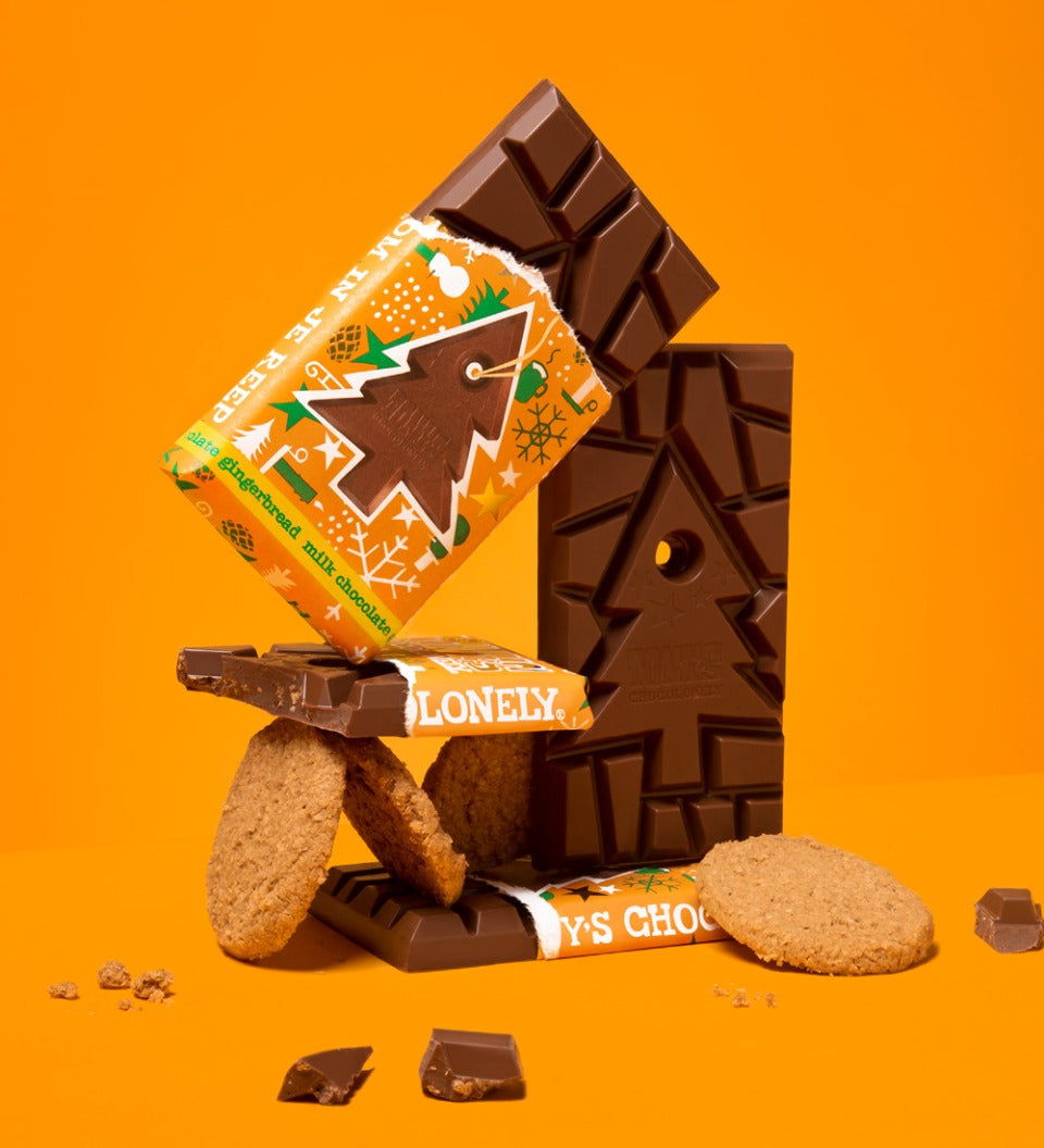 3 Tony's milk chocolate gingerbread bars stacked in a pile with some gingerbread biscuits on an orange background