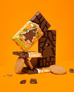 3 Tony's milk chocolate gingerbread bars stacked in a pile with some gingerbread biscuits on an orange background