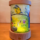 Spring Toverlux lantern shade with gnome tales artwork by Mhairi Hellbrandt  featuring a blue tit bird displayed in a lit lantern.