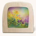 A Toverlux silhouette in the magic lamp, the illustration is of some purple flowers and daffodils with a dreamy purple and green gradient sky in the background.